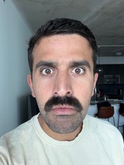A man with a mustache and wide, surprised eyes staring directly at the camera.
