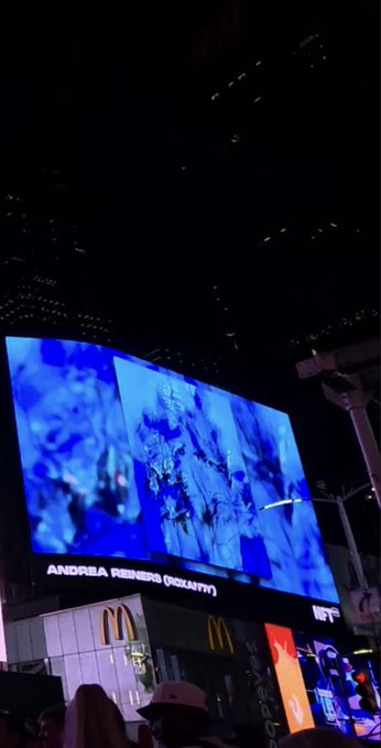 A nighttime photo of a large digital billboard displaying blue-tinted imagery with the text "ANDREA RENEWS (IDENTITY)" above a McDonald's sign.