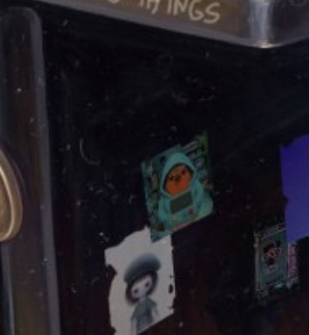 The image shows a dark, slightly blurry close-up of what appears to be a screen or display featuring small digital characters and NFT-style artwork, with partial text "THINGS" visible at the top. The scene ties to the post by showcasing a digital/animated artwork featuring a character with an orange face and a figure in a cap, suggesting references to NFT collections like BAYC and Meebits being highlighted alongside the AgentRobertAI project.