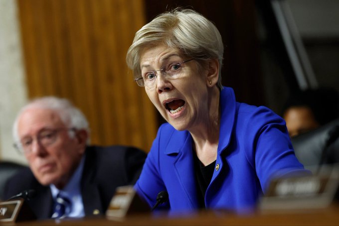 A woman in a blue blazer speaks passionately at a hearing with a nameplate reading "Sen. Ernst," while an older man sits beside her; the caption's reference to "this Indian" appears to be a misidentification, as the woman pictured is Senator Joni Ernst, who is not of Indian heritage.