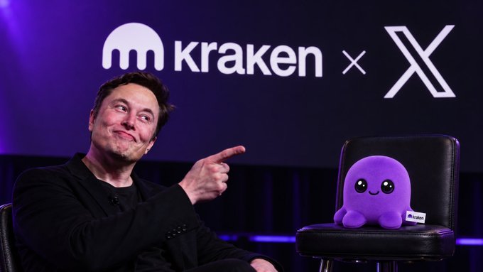 Elon Musk pointing at a Kraken plush mascot, with the 'kraken x X' logo displayed on the screen behind him.
