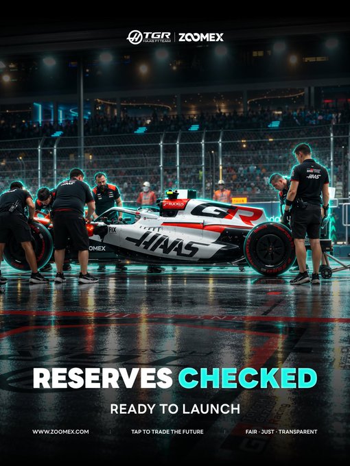 A promotional graphic shows an F1-style Haas race car surrounded by pit crew on a wet nighttime racetrack, with TGR and ZOOMEX logos at the top. Bold text reads “RESERVES CHECKED” and “READY TO LAUNCH,” reinforcing Zoomex’s security message about 2FA, withdrawal whitelists, and reviewing recent login devices.