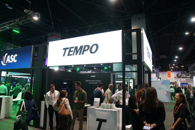 A busy trade show floor with a prominent illuminated 'TEMPO' booth, alongside an 'ASC' booth, where numerous attendees are networking.