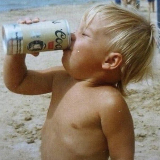A vintage-style photograph of a young blonde child drinking from a large can of Coors Light beer while standing on a sandy beach.