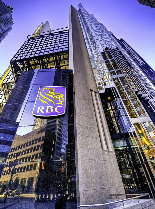 A low-angle photograph of a modern glass skyscraper featuring a prominent RBC (Royal Bank of Canada) shield logo mounted on its exterior facade.