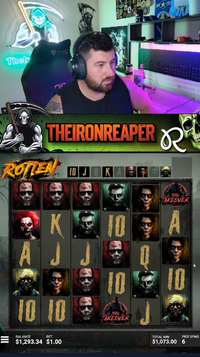 The image shows a man sitting at a slot machine, wearing headphones and looking focused as he plays. The slot machine has a variety of symbols displayed, including a skull and crossbones symbol, which adds an element of mystery or excitement to the game. The surrounding environment appears to be a casino setting with other people present in the background.