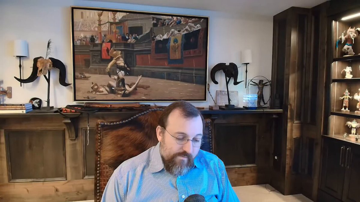 The image features an office setting with a man sitting at his desk using a computer mouse. The room has a large painting of a man on a horse as well as several other objects, including a chair, a couch, and various figurines. There are also two lamps in the scene - one near the center of the room and another closer to the right side.