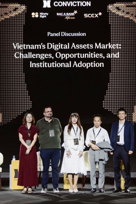 A panel discussion photo featuring five people standing on stage at a Conviction event, with the screen behind them reading 'Vietnam's Digital Assets Market: Challenges, Opportunities, and Institutional Adoption' alongside logos for Ninety Eight, BAC A BANK, and SCCEX.
