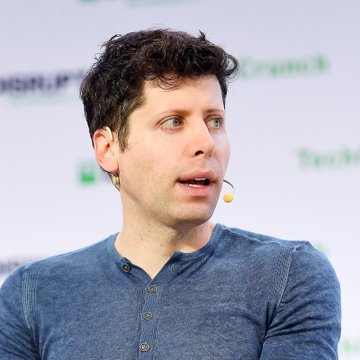 A man with curly dark hair, wearing a blue henley shirt and a headset microphone, appears to be speaking at what looks like a TechCrunch Disrupt event (partial text "rupt" and "Tech" visible in the background). The image aligns with the post's commentary on AI's communication challenges, as the speaker—likely a tech industry figure—visually represents the "builders" mentioned who are working to bridge the gap between technical capabilities and public understanding in the AI space.