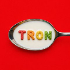A silver spoon holds white milk with colorful letter-shaped cereal spelling out the word 'TRON' against a solid red background.