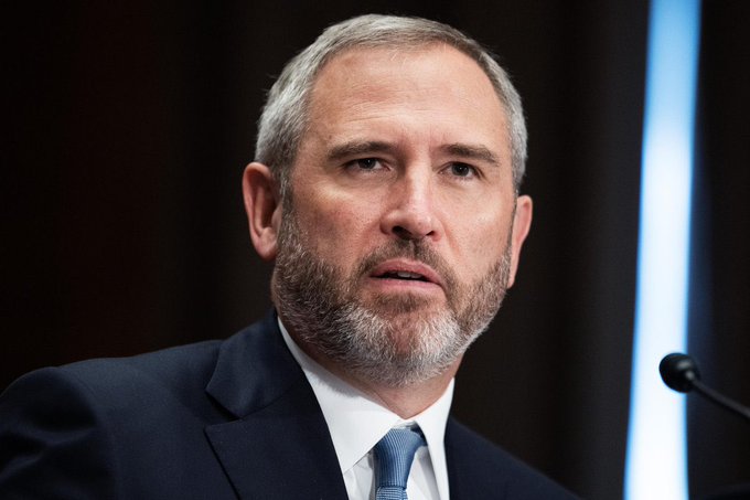 The image shows a man wearing a suit, tie, and beard speaking into a microphone at a podium. He appears to be delivering a speech or presentation. The caption below the photo reads "Buy the fucking dip $XRP". This phrase is likely an inside joke or reference to Bitcoin, which has been used as slang for "bitcoin" in recent years.