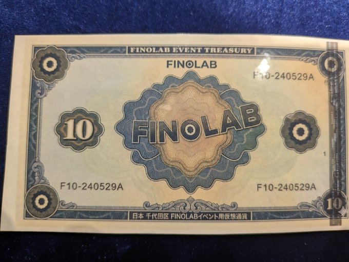 A "FINOLAB EVENT TREASURY" note worth 10 units, serial number F10-240529A, representing a physical cryptocurrency-style voucher issued for the Finolab event.
