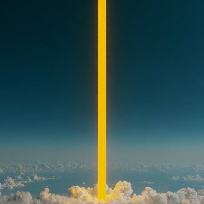 A bright yellow beam of light shoots vertically up into a blue sky filled with white clouds, creating a dramatic, surreal scene.