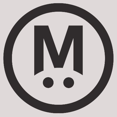 A light gray square logo featuring a black circle containing a stylized letter 'M' with two dots beneath it.