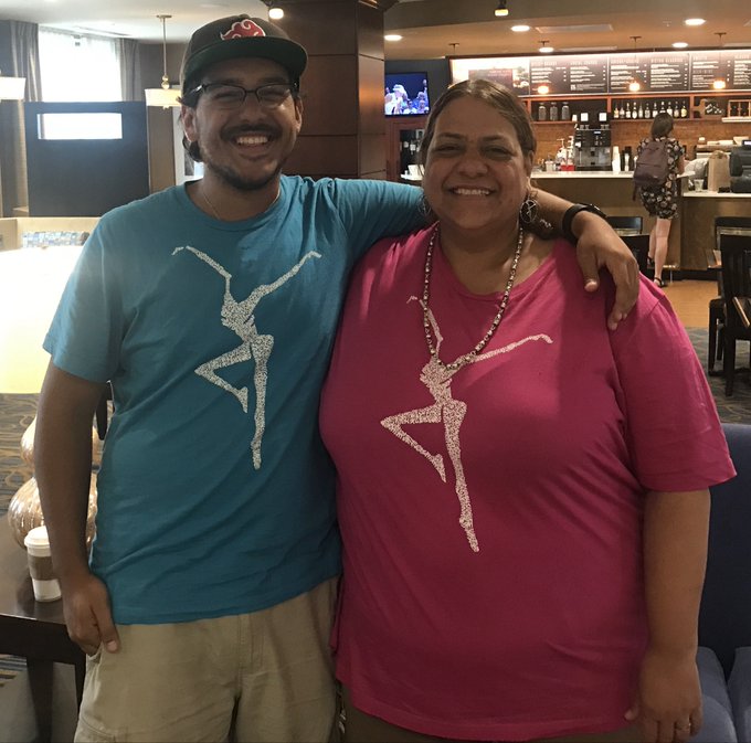 A man and a woman smiling and posing together, both wearing t-shirts featuring a dancing skeleton graphic, inside a coffee shop.