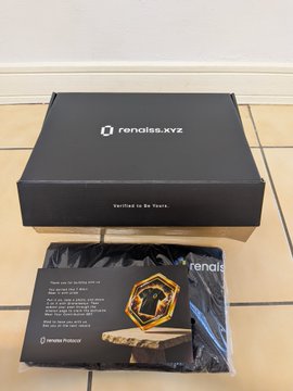 A black shoebox branded "rendliss.xyz" with the tagline "Verified to Be Yours" sits on a tiled floor next to a black package containing a gold-colored accessory, possibly a belt buckle, with a certificate of authenticity.