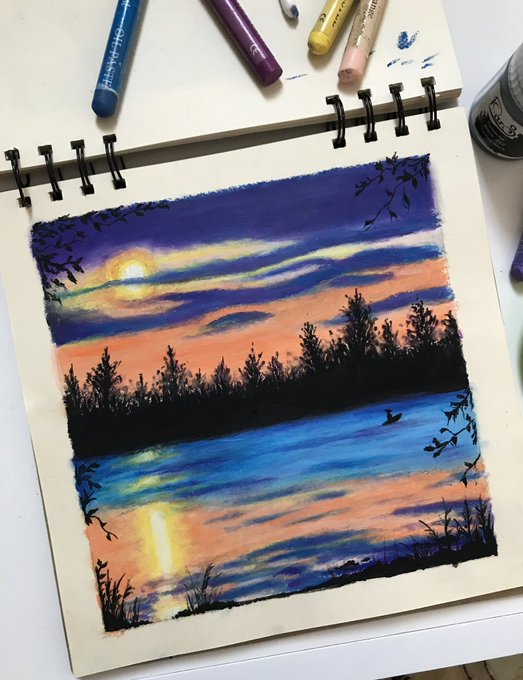 A sketchbook open to a colorful pastel drawing of a sunset over a lake with silhouetted trees, with oil pastels visible at the top of the page.