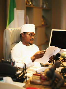 This image shows Senator-elect Abdullahi Bello, dressed in traditional attire, reviewing documents. The post confirms this is an "INCOMING SENATOR" in preparation for his new role.