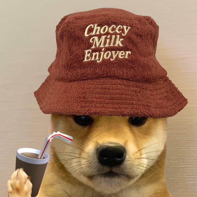 A Shiba Inu dog wearing a brown towel bucket hat embroidered with "Choccy Milk Enjoyer" while sipping chocolate milk through a striped straw, perfectly embodying the "enjoyooor" vibe.