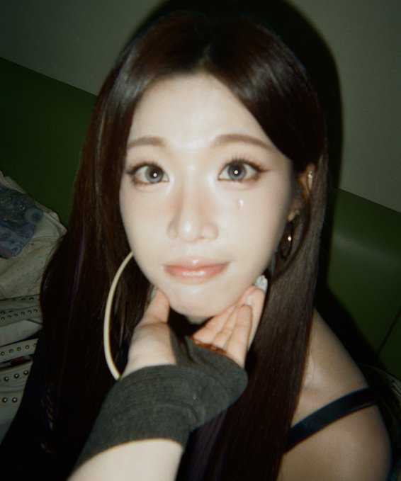 A close-up selfie of a young woman with long dark hair, posing with her hands near her chin.
