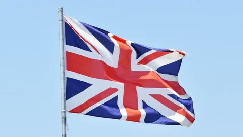 The Union Jack flag of the United Kingdom waves against a clear blue sky, visually representing the UK government in connection with the news that Crypto APPG co-chairs Gurinder Singh Josan MP and Lord Vaizey have written to major bank CEOs seeking clarity on their approach to crypto firms and transactions under the UK's new regulatory regime.