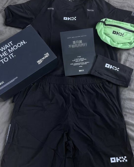 A flatlay shows a black OKX-branded t-shirt and shorts, a neon green waist pack, a black drawstring pouch, and a black gift box reading "WAIT THE MOON, TO IT" with "NEW. THE MOON. APP" and a card wishing "等月圆 不如向月而行" — matching the caption's mention of a surprise OKX Mid-Autumn gift box filled with thoughtful, high-quality branded merchandise.