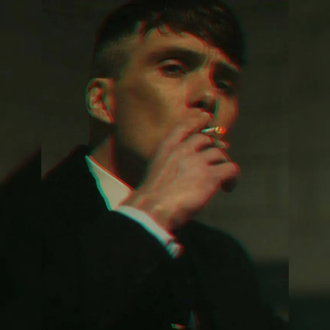 The image shows Thomas Shelby, played by Cillian Murphy, smoking a cigarette in a dimly lit scene that has been altered to give him a swollen, puffy face—reflecting the post's theme of resilience and defiance, mirroring how the poster is doubling down on their bullish stance on the $ANSEM token despite its volatility. The character's steely expression complements the tone of the tweet, emphasizing the message of pushing through market "nukes" with confidence.