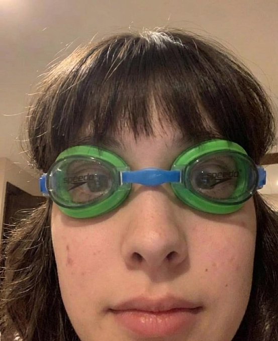 A close-up selfie of a person wearing bright green Speedo swimming goggles with a blue strap.