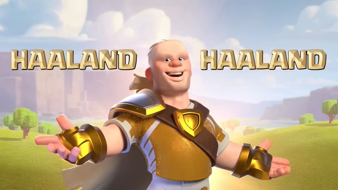 A 3D animated blonde character with a blonde ponytail in gold and white armor stands smiling with open arms in a grassy field, with "HAALAND" written in bold gold letters on both sides of his head. The image playfully references footballer Erling Haaland's name, edited onto a Clash of Clans-style warrior to suggest a partnership between Mavia Game and Haaland similar to in-game collaborations.