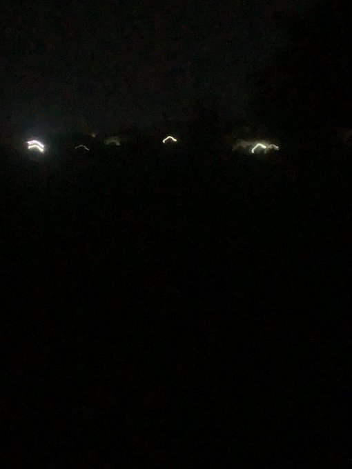 A dark nighttime photo showing a row of small, distant lights along what appears to be a horizon or elevated ridge.