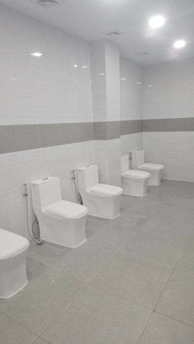 A row of four white toilets lined up in a clean, modern public restroom with gray and white tiled walls. The image humorously plays on the "sh*tcoins" pun, fitting the degen crypto humor referenced in the post.