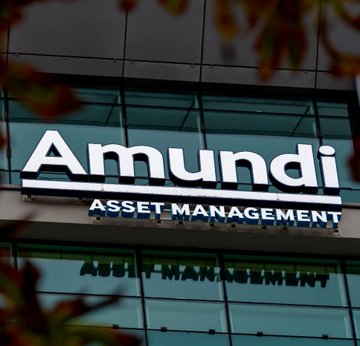 The image shows the exterior signage of "Amundi Asset Management" mounted on a glass building façade, with blurred autumn foliage in the foreground. The sign relates directly to the news that Amundi, Europe's largest asset manager, has significantly increased its holdings in Michael Saylor's Strategy (MSTR) to approximately $125 million.