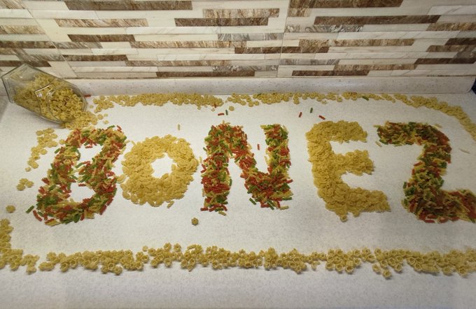 The word "DONER" is spelled out on a white countertop using pasta and vegetables, with a jar of pasta poured out beside it.