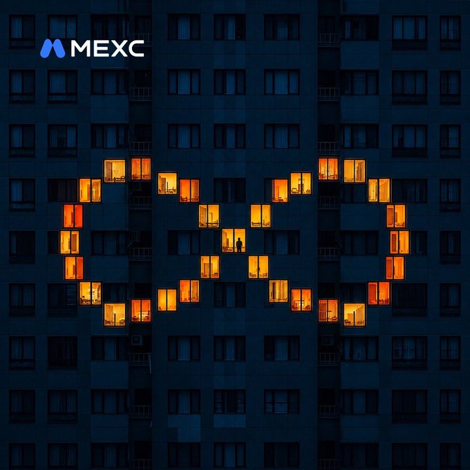 The image shows the facade of a dark high-rise apartment building at night, where the illuminated windows form the MEXC logo, with the "M MEXC" text displayed in the upper left corner. The glowing orange lights create a pixelated logo pattern across the building's grid of windows, visually celebrating the MEXC brand referenced in the post about their improved team performance.
