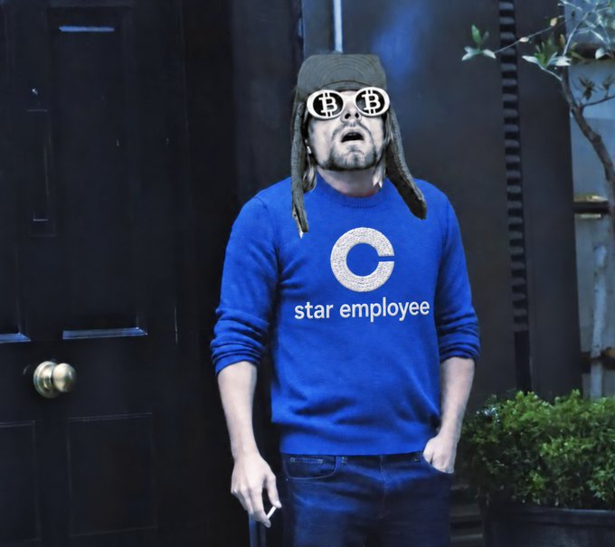 A man wearing a blue sweater reading 'C star employee' stands outside a dark door, wearing a fur hat with ear flaps and Bitcoin-logo sunglasses, holding a cigarette.