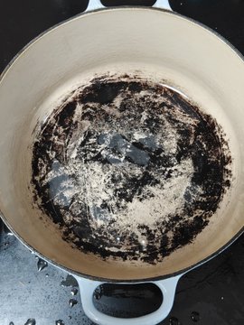 A dirty, stained Dutch oven or pot with burned residue on the bottom, viewed from above.