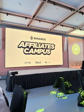 An empty event room set up for '**BINANCE AFFILIATES CAMPUS**' with sponsor logos (OSL, others) visible on the screen and side wall.