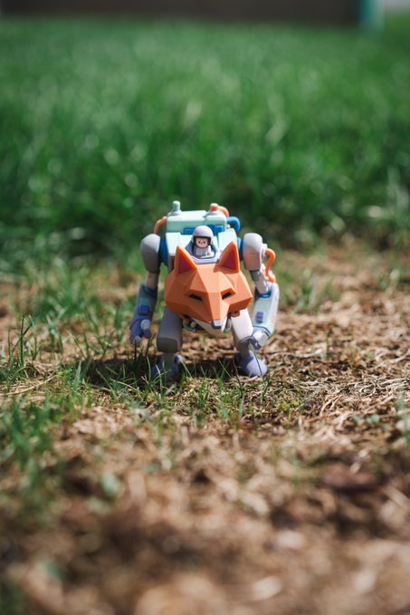 A small mech-style robot toy with an orange fox-like mask and a pilot figure stands on a grassy patch, matching the post's "MECHAMASK: OPERATIONAL" caption celebrating a toy received from @doodles.