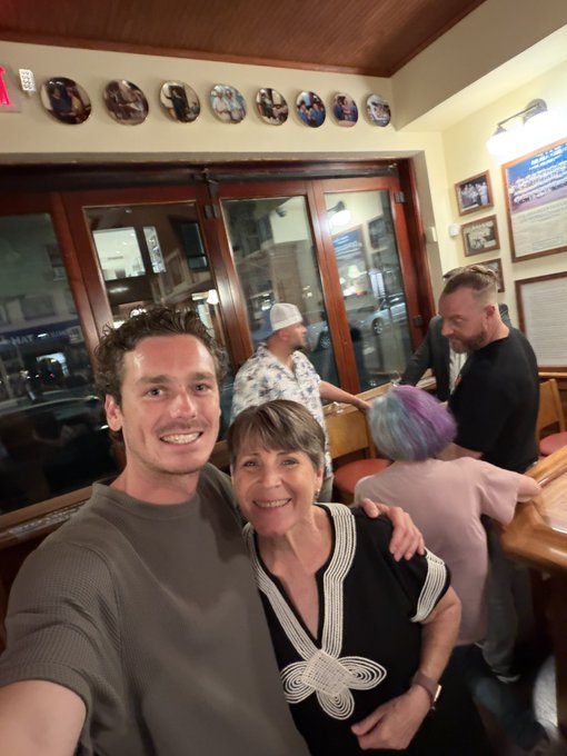 A man and an older woman smiling for a selfie in a restaurant decorated with plates on the walls.