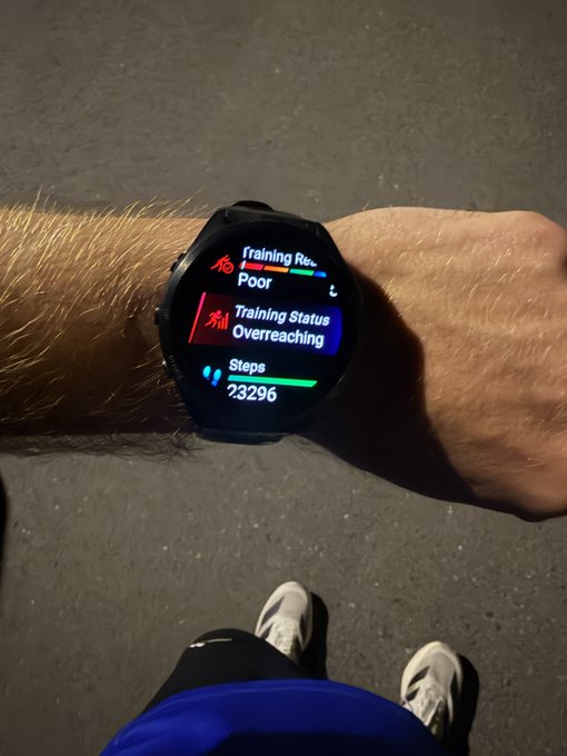 A smartwatch displays fitness metrics including 'Training Recovery: Poor', 'Training Status: Overreaching', and 'Steps: 23,296'.