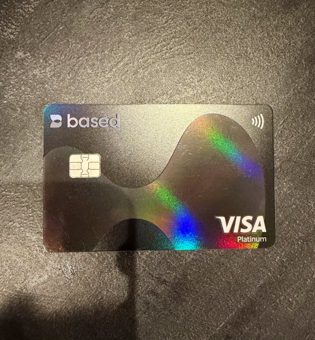 A holographic "Based" Visa Platinum debit/credit card rests on a gray surface, its iridescent design catching light in vibrant rainbow hues. The post humorously contrasts keeping this "rare card" as a keepsake while still waiting for a gold version to arrive.
