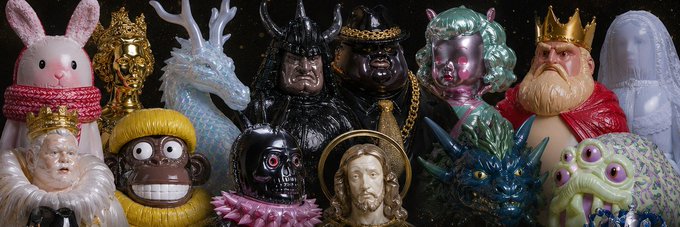 A collection of various colorful designer art toys and figurines, including a pink bunny, a golden figure, a white dragon, dark warriors, a bearded king, and other character sculptures, is displayed together against a dark background.