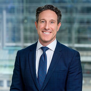 A professional headshot of a smiling man in a navy blue suit and patterned tie, likely Ryan VanGrack, the Coinbase vice chair referenced in the post about the CLARITY Act being close to passage.