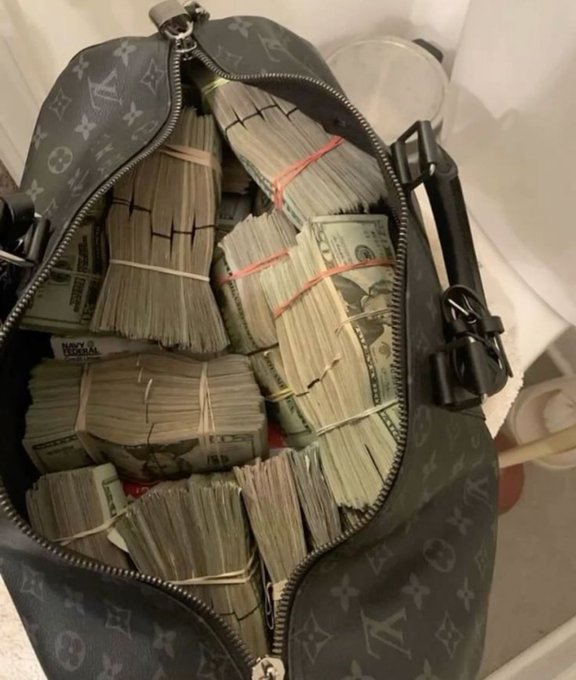 An open Louis Vuitton monogram duffle bag filled with numerous rubber-banded stacks of US currency bills.