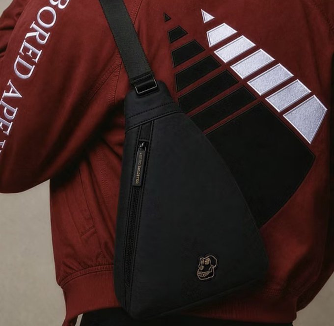 A close-up of a person wearing a maroon jacket with a triangular graphic and the partial text 'BORED APE', carrying a black triangular sling bag with a small monkey logo patch.