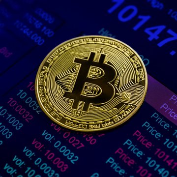 A golden physical Bitcoin coin rests atop a digital trading screen displaying price figures like "10147" and volume data, visually representing the cryptocurrency's market activity. The image complements the post about declining dormant Bitcoin movements and reduced selling by long-term holders, highlighting the underlying asset at the center of the latest on-chain data from Galaxy.