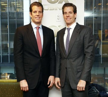 The image shows two men posing for a picture, both dressed in suits and ties, which suggests they are professionals or attending a formal event. A poster with the title "FOX BUSINESS" is visible behind them, indicating that this is likely an office environment where such events occur. In the background of the image, there's another person who might be related to the business or attending the same event. The post displays some intriguing facts about Bitcoins and mentions a significant amount of money involved in Bitcoin trading, possibly worth $11 million in 2019 and now valued at almost $11 billion, making it one of the most successful trades of the century.