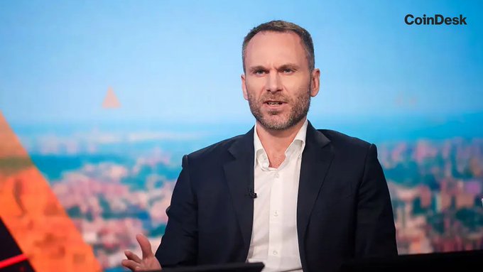 Paolo Ardoino, CEO of Tether, speaks on a CoinDesk segment explaining why the company declined to pursue a MiCA license due to the regulation's reserve requirements. He is shown in a dark blazer and white shirt against a backdrop of a cityscape and desert landscape.