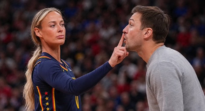 A blonde woman in a navy USA jersey (number 11) holds her finger to the lips of a man in a gray sweater, illustrating the "hush" sentiment expressed in the caption about Ledger requiring clear signature approvals before anything gets signed.