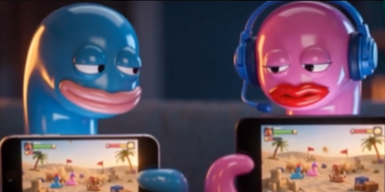 Two colorful glossy figurines, one blue and one pink wearing headphones, holding smartphones and appearing to play a desert-themed mobile game.